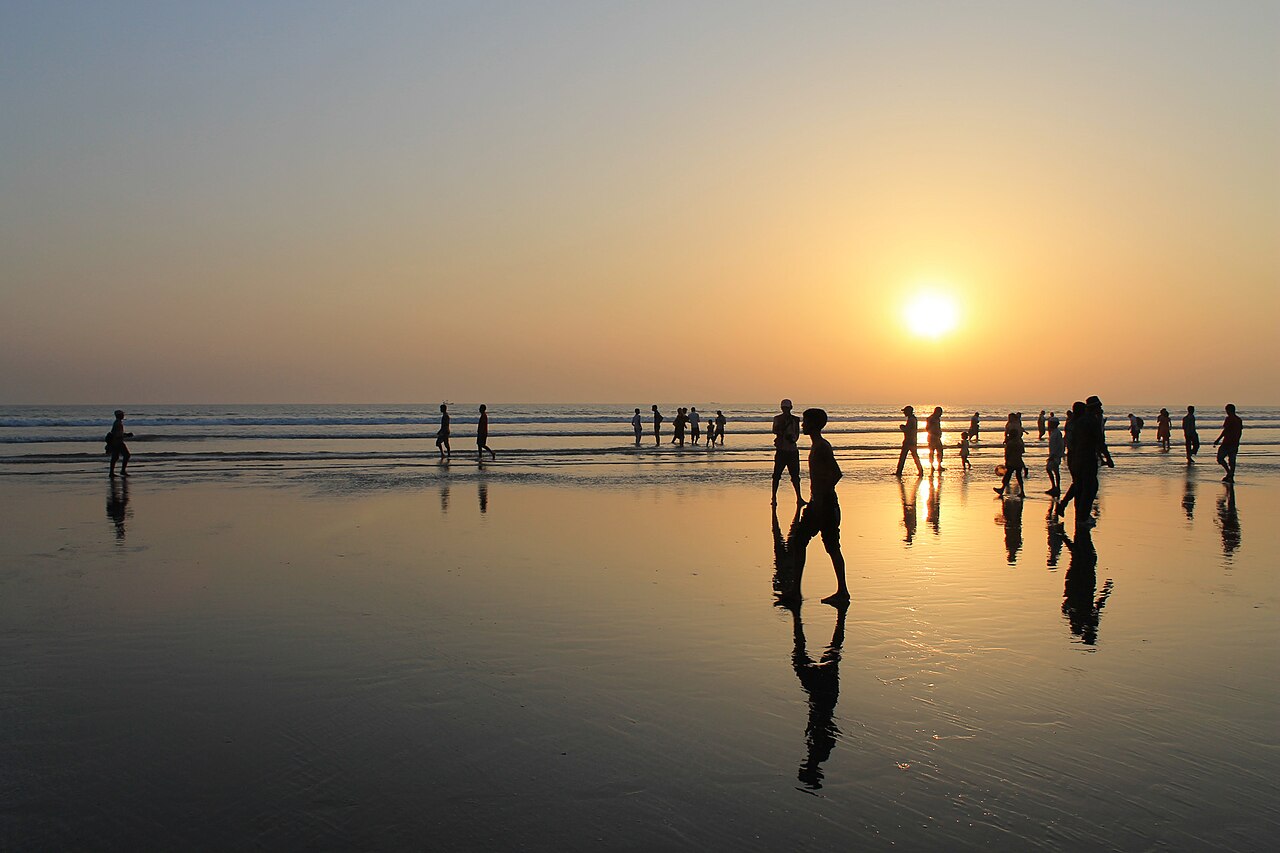 People walking on wet sand at Cox's Bazar beach at sunset