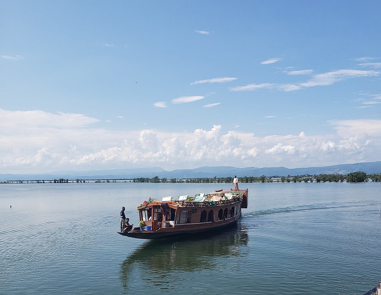 A wooden houseboat on the open water of Tanguar Haor under a blue sky